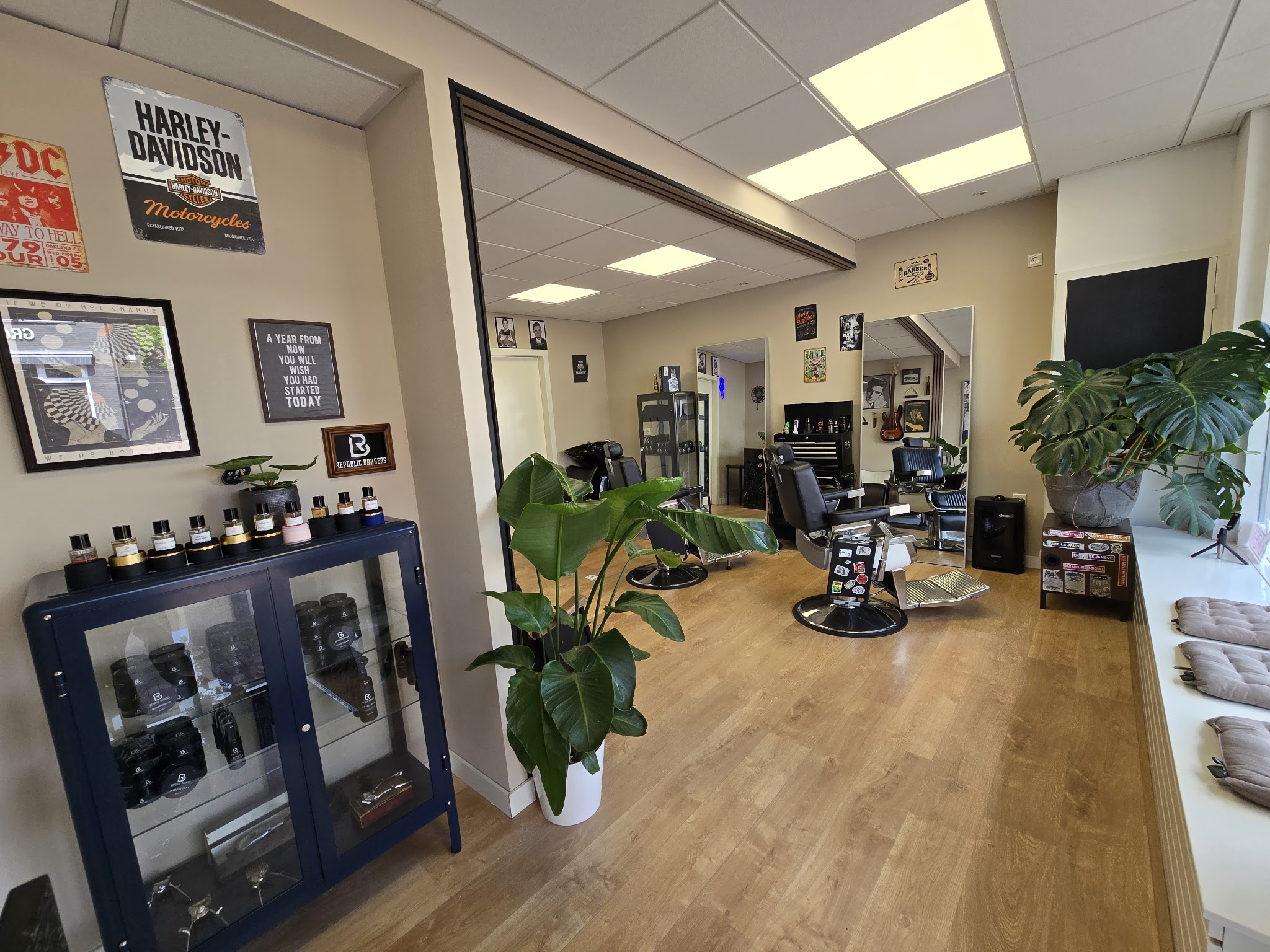 De shop van binnen: stoelen, spiegels, planten, houten vloer en een vitrine met Republic Barbers producten