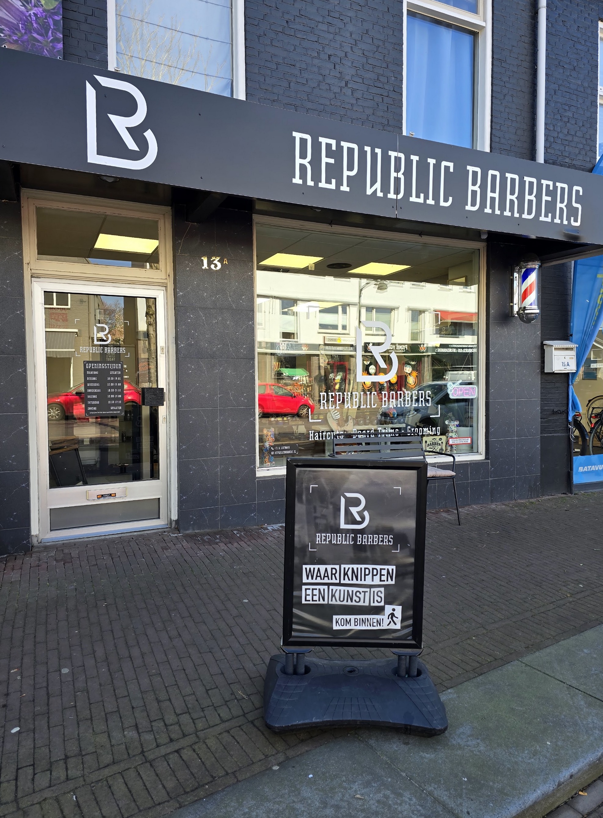 De zwarte gevel van Republic Barbers met het uithangbord en een stoepbord voor de deur
