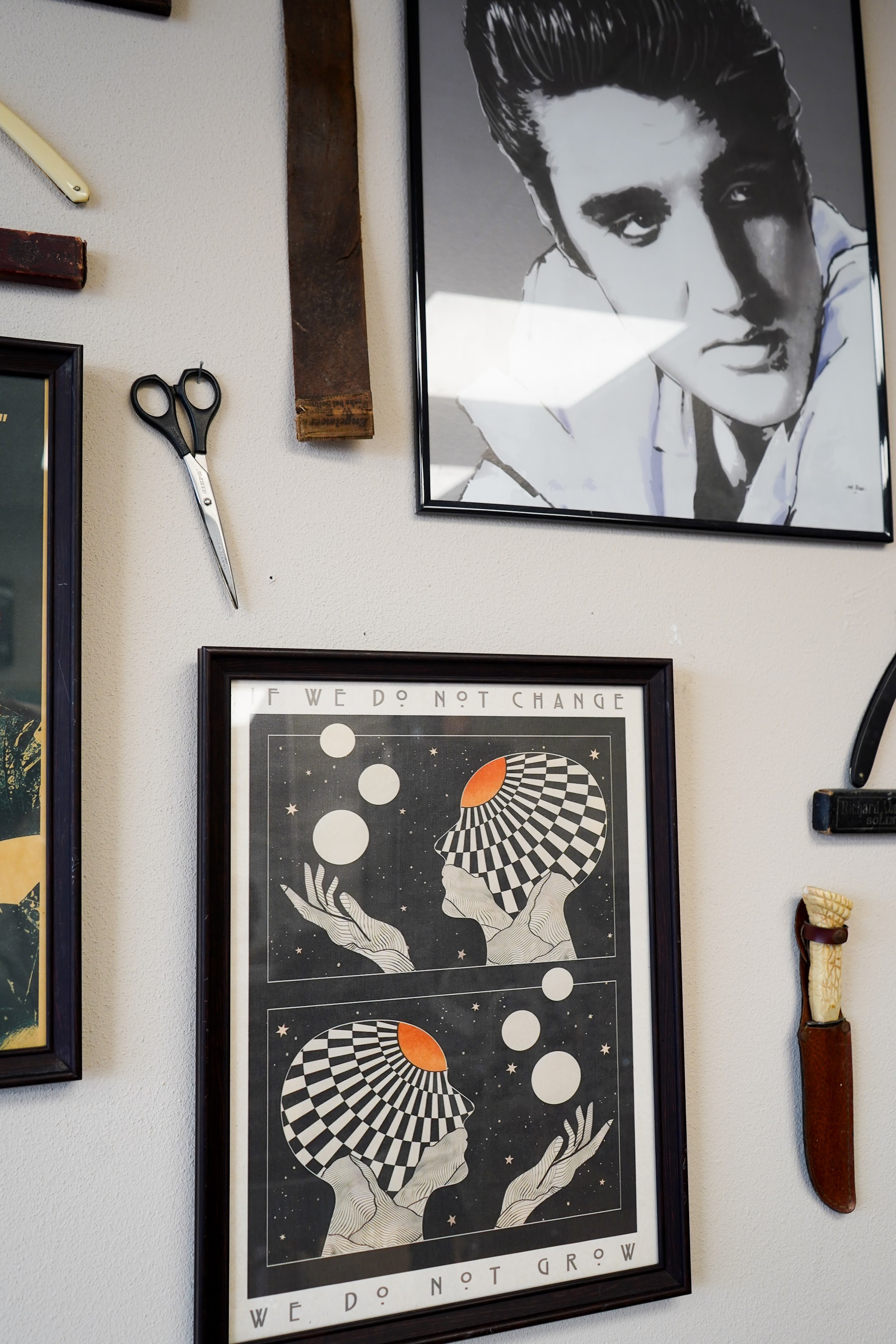 Wanddecoratie in de shop: ingelijste prenten, een schaar, een scheermes en een portret van Elvis
