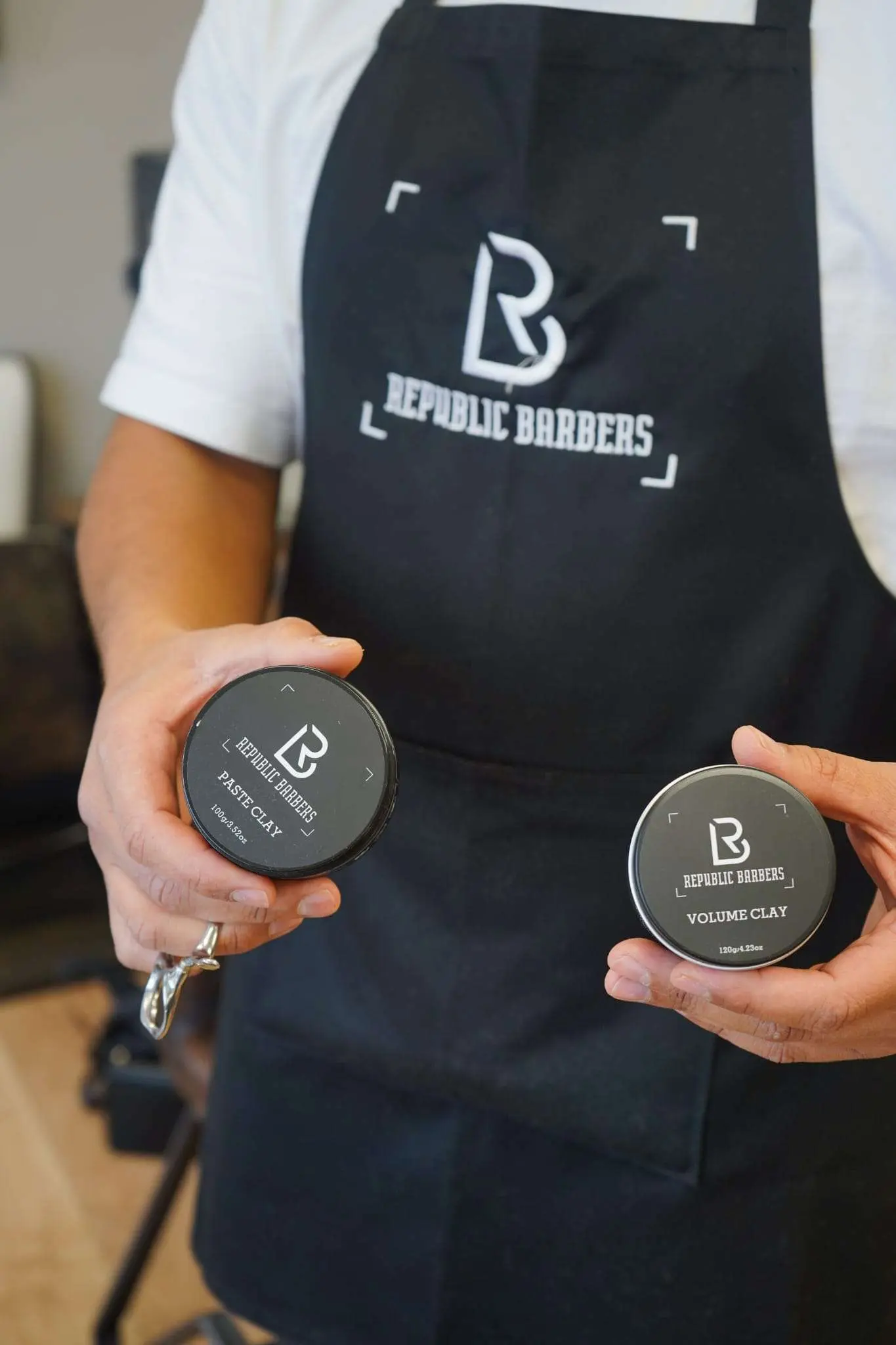 Barber in zwart Republic Barbers schort met twee potjes clay van het eigen merk